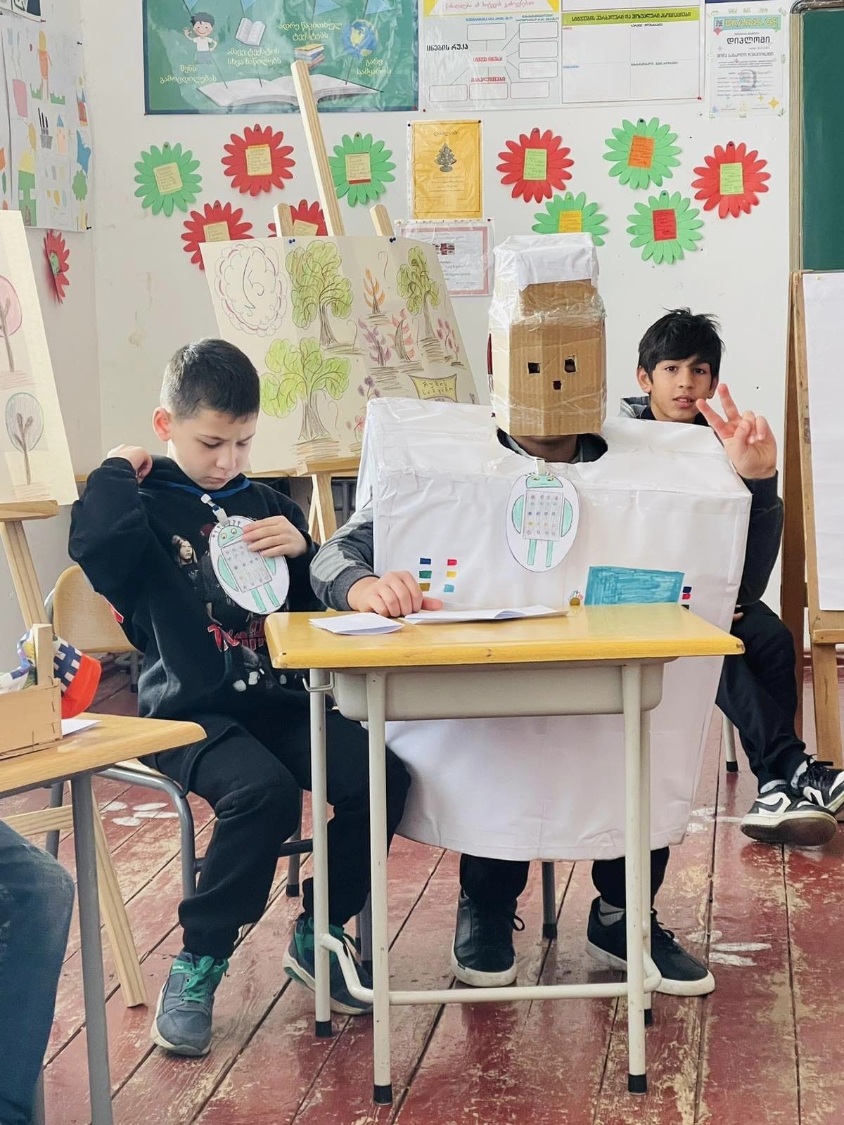 Kuvassa voi olla 3 henkilöä, opiskelijat, lelu ja teksti