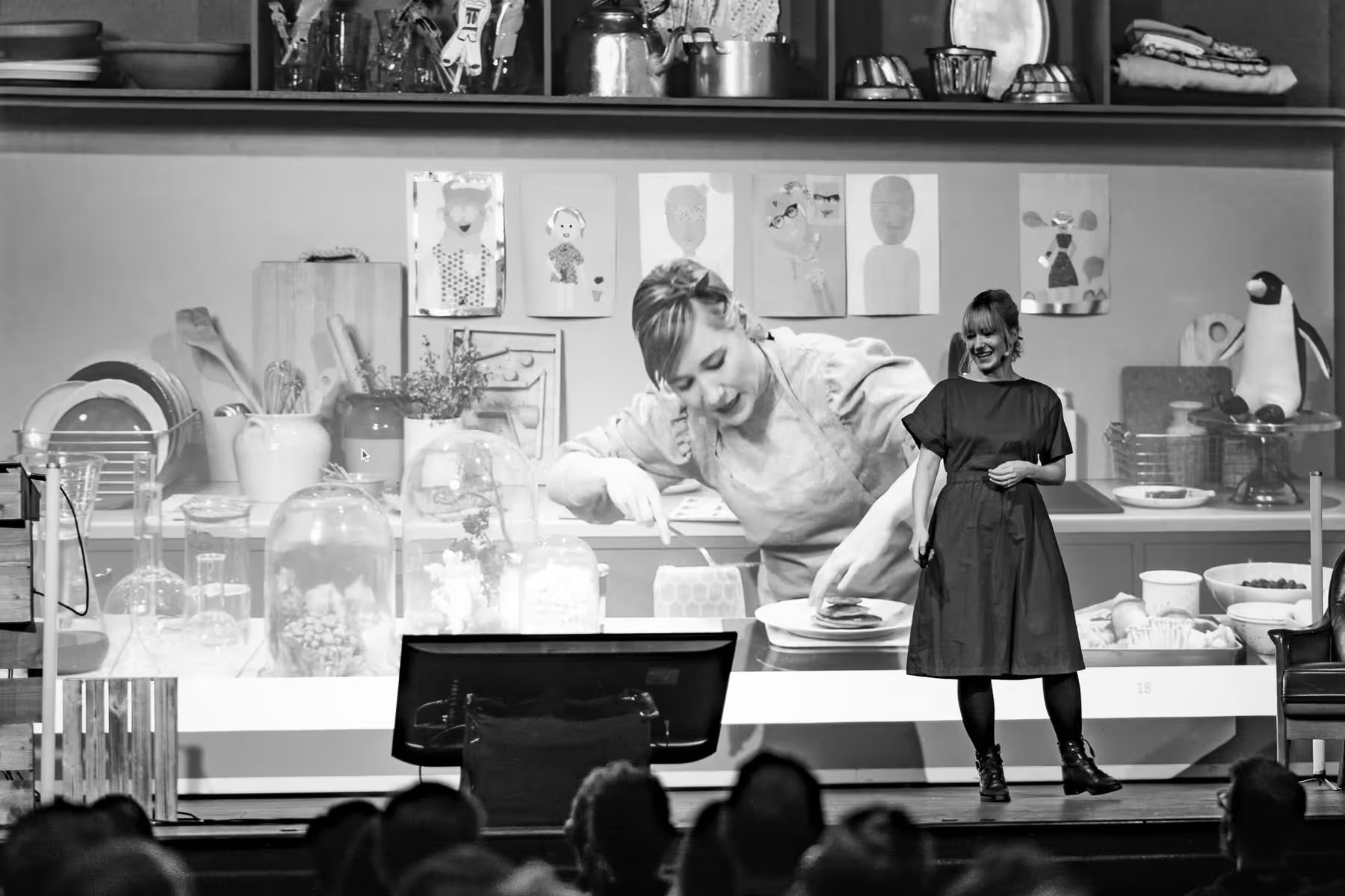 Linda Liukas on stage in front of a large slide showing a baker decorating pancakes, surrounded by chemistry beakers, child drawings and kitchenware.