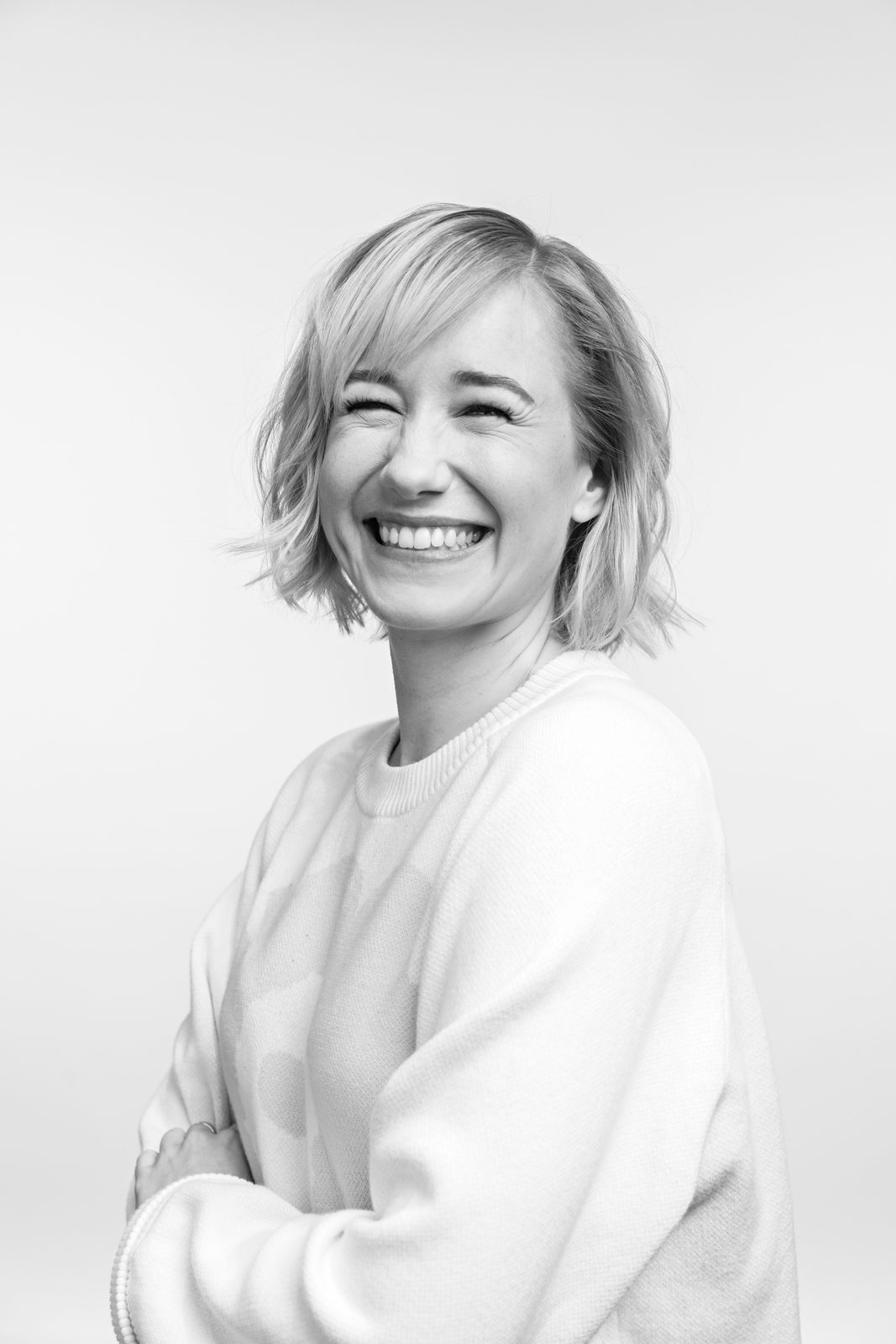 Black-and-white studio portrait of Linda Liukas laughing, arms folded, against a pale background.