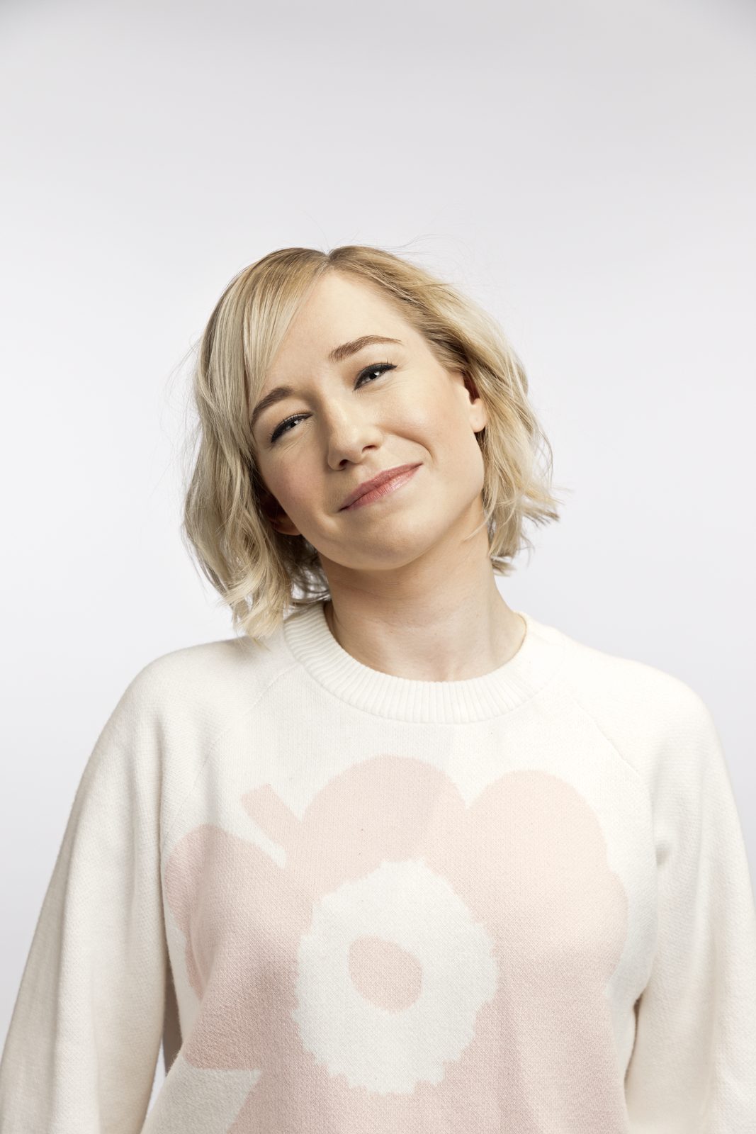 Studio portrait of Linda Liukas in a cream Marimekko Unikko jumper, head tilted, against a pale background.